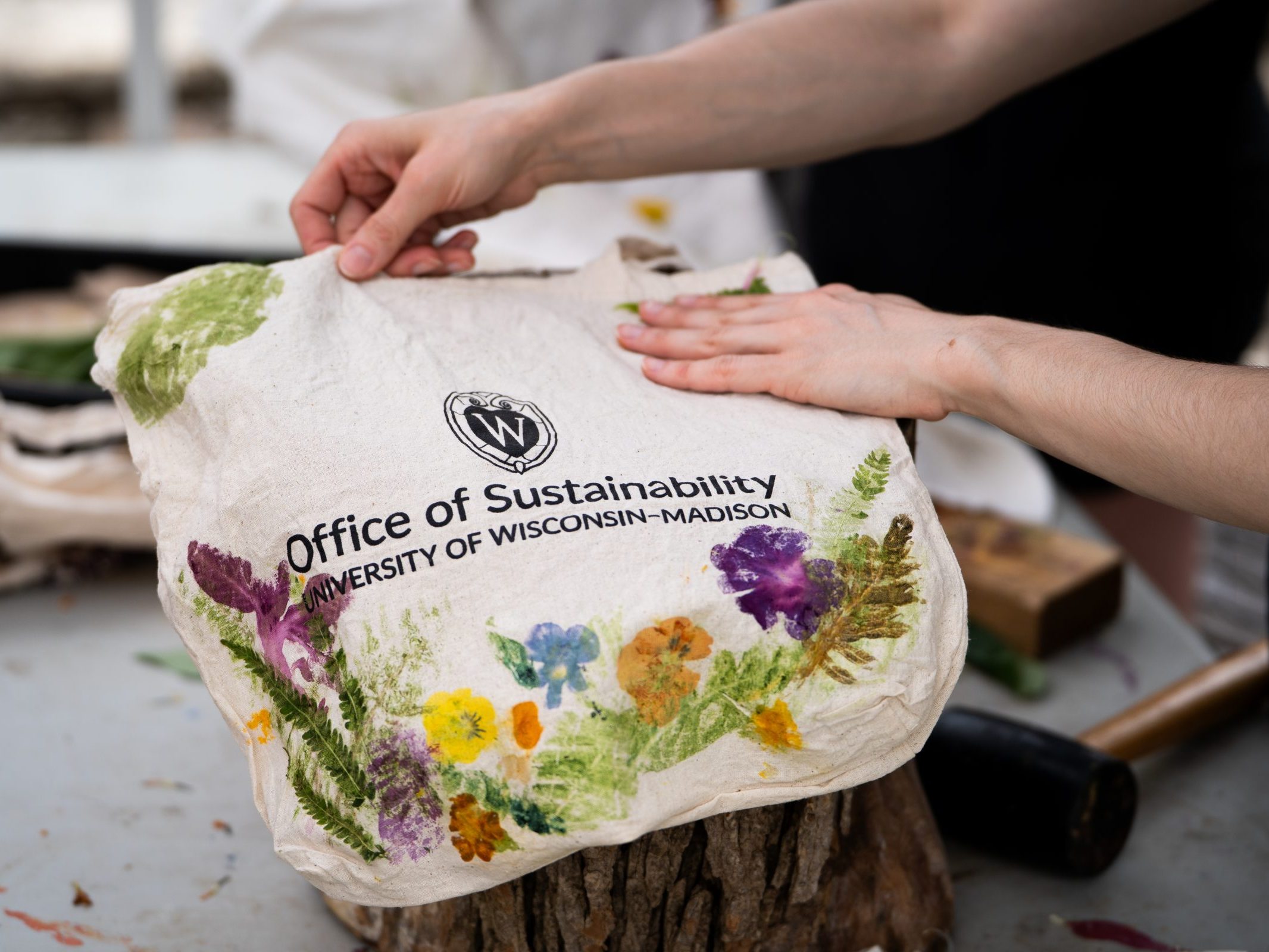 Someone making a bag with the UW Office of Sustainability logo with flower edging