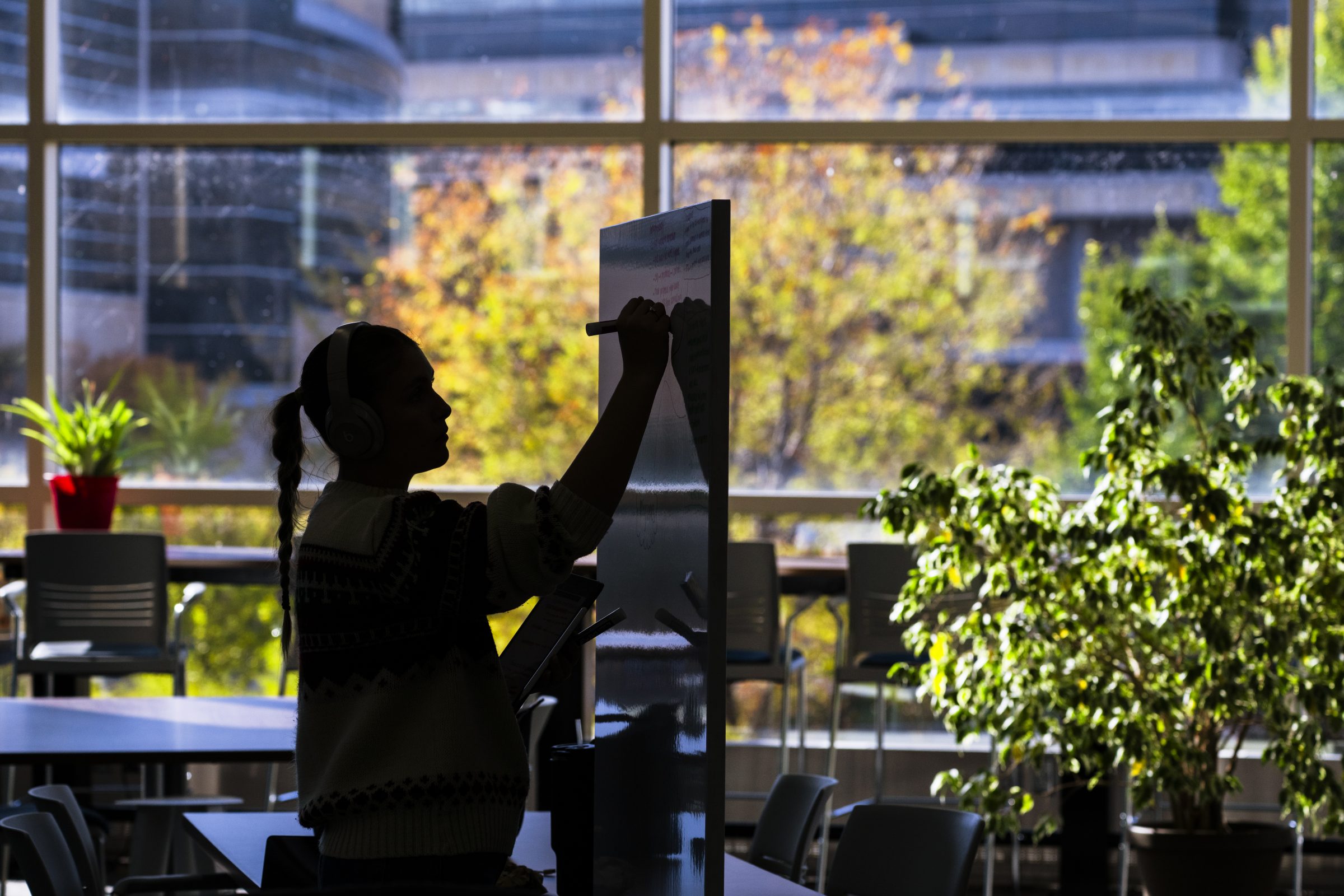A woman standing at a white board writing.
