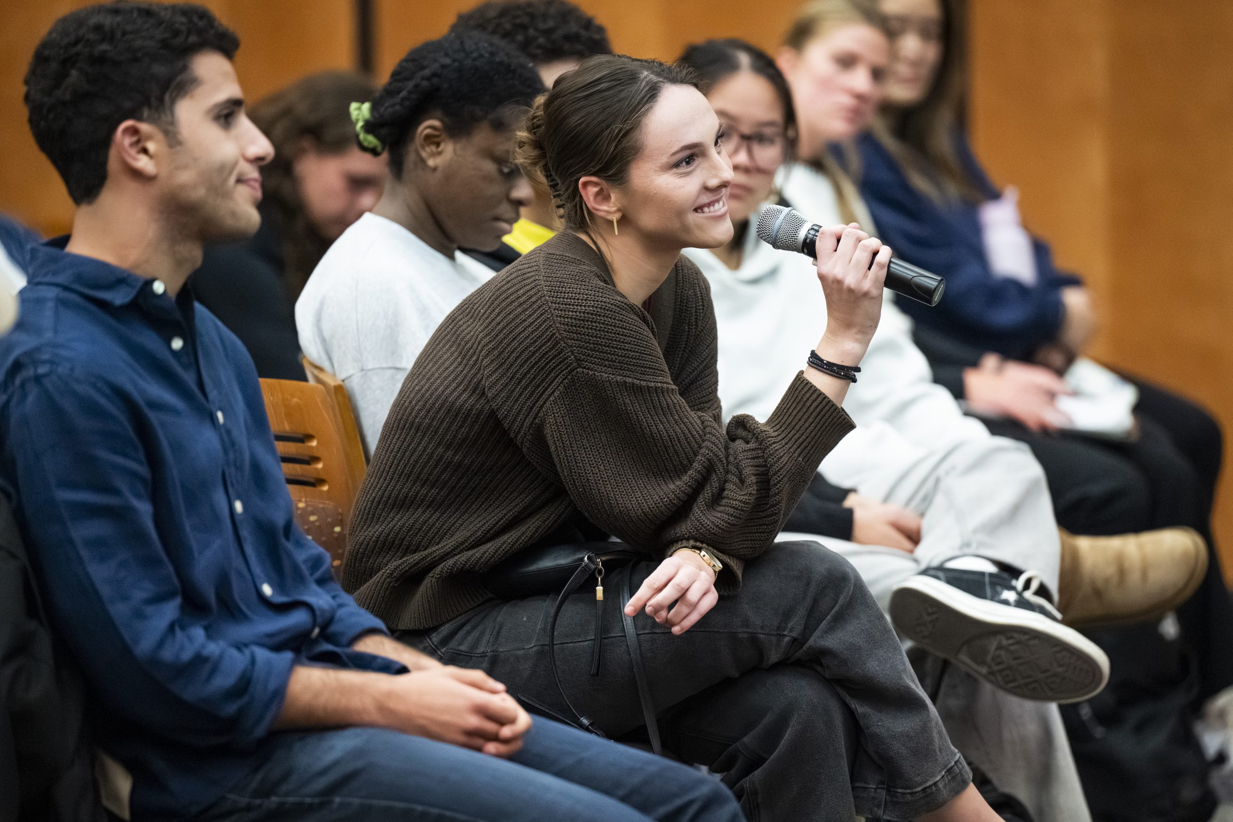 A group of college students with one of them holding a microphone asking a question.