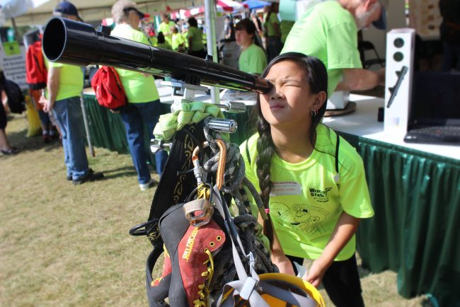 Girl looking through a telescope at an outdoor event. 