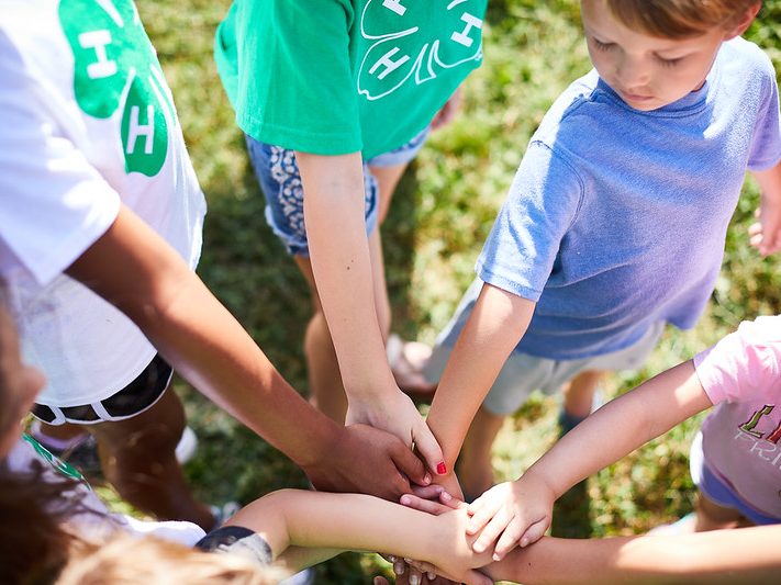 4-H kids all in a circle with their hand on top of each other in the center.