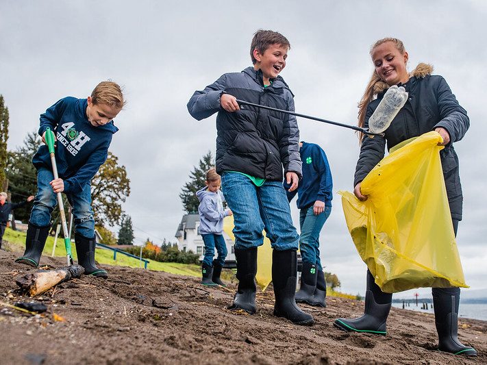 Kids on a beach putting garage into bags.