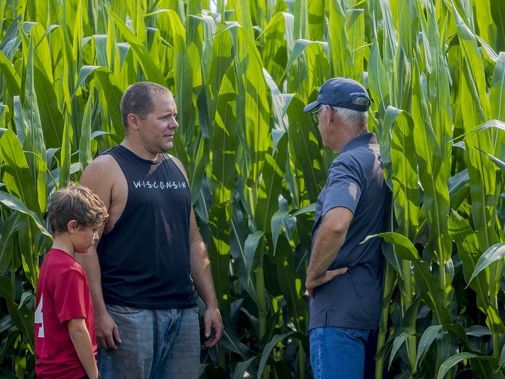 Three generations on a farm in front of corn.