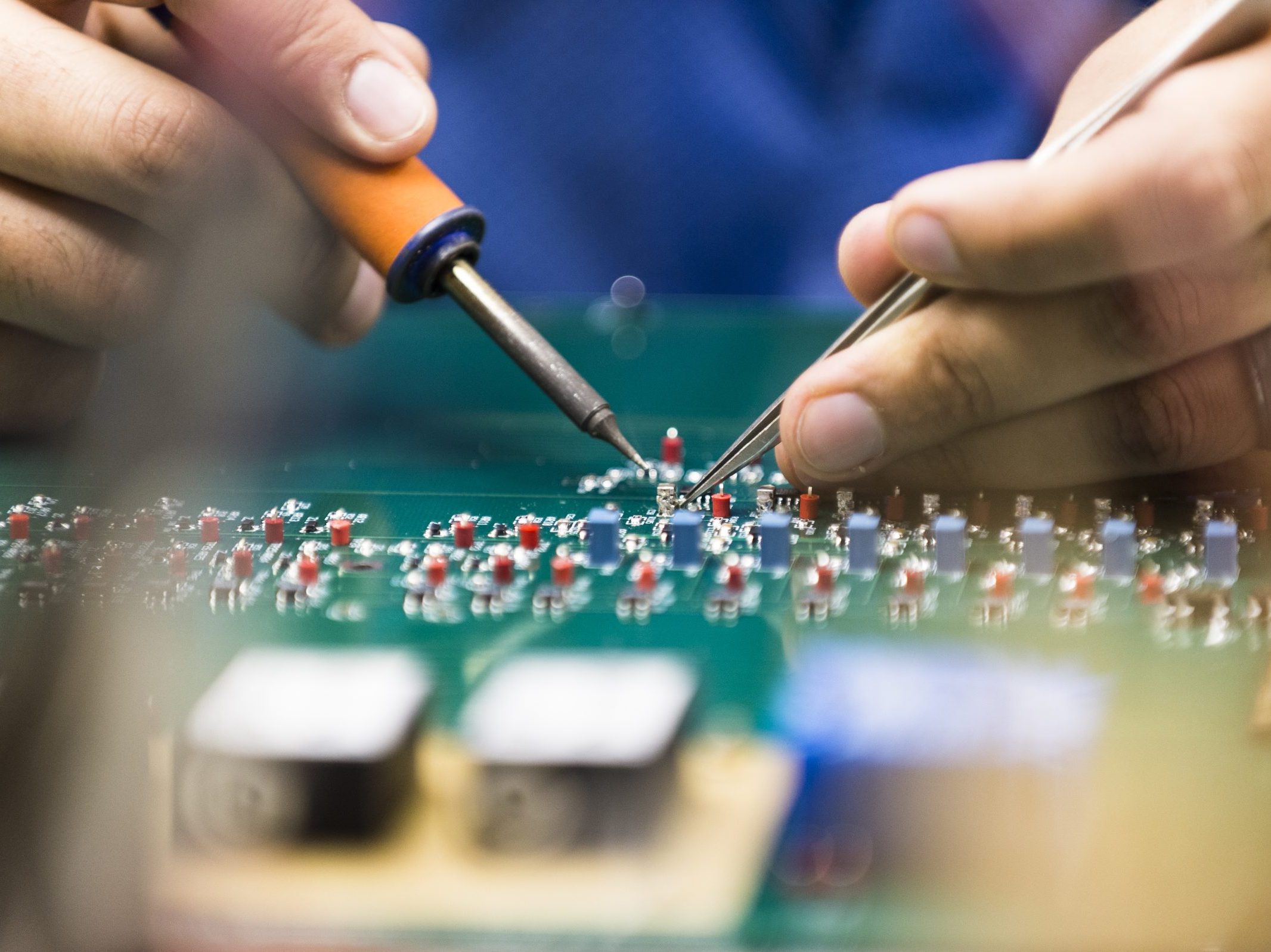 Hands with tools soldering a circuit board.