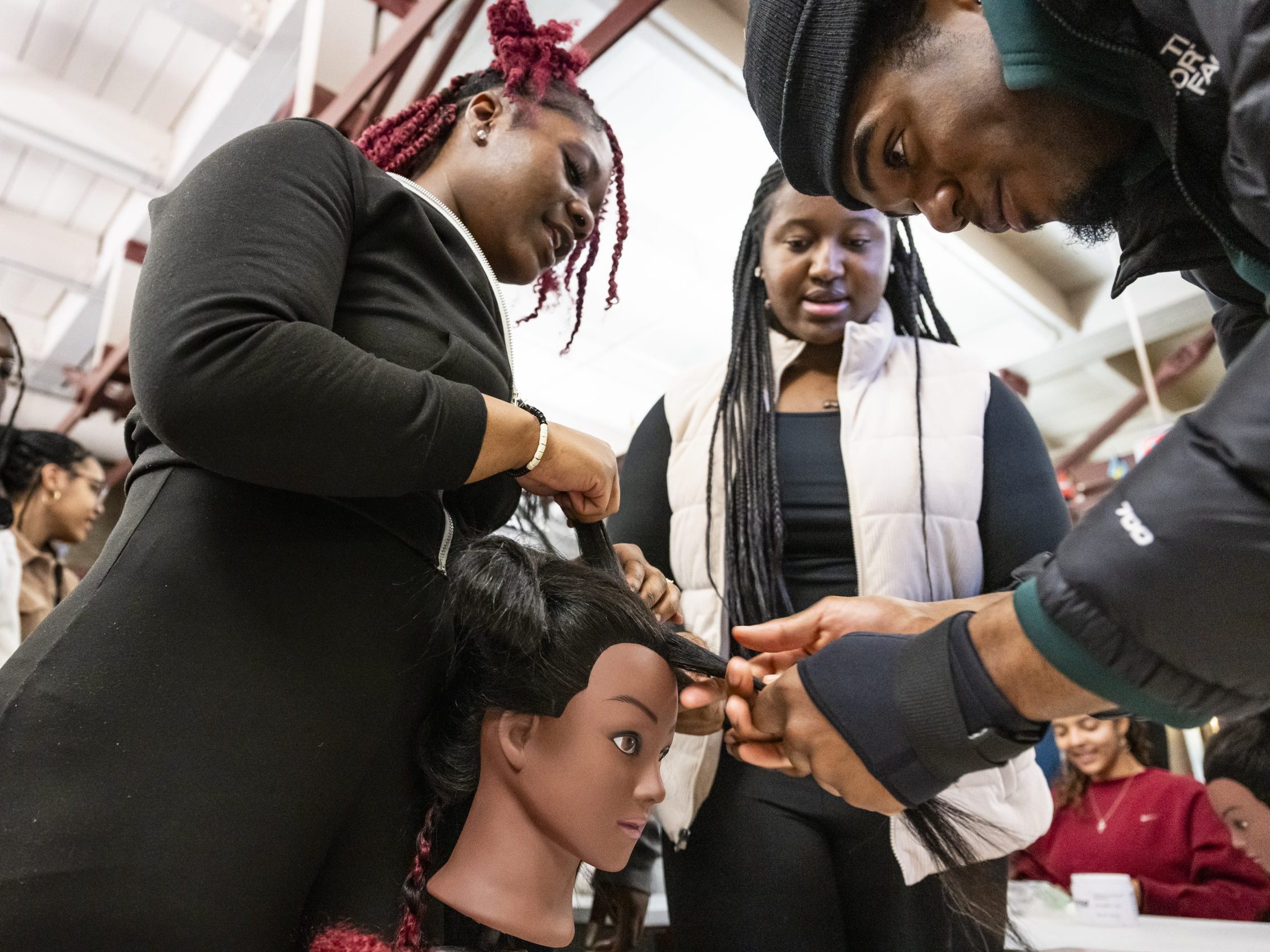 Two girls watching a man cutting hair off of a mannequin head.