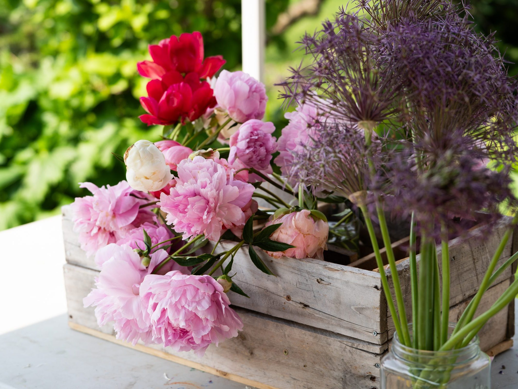 Pink and red cut flowers in a wood box and purple flowers in a glass jar.