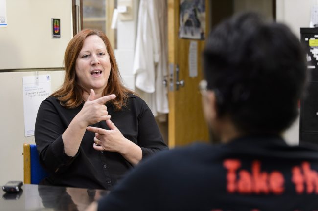Woman using sign language with a man sitting in front of her