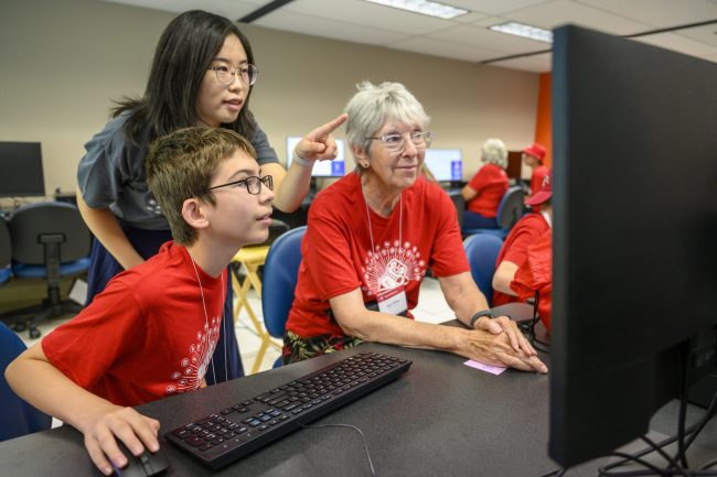 A young boy at a computer with an older woman and a young teacher pointing at the monitor.