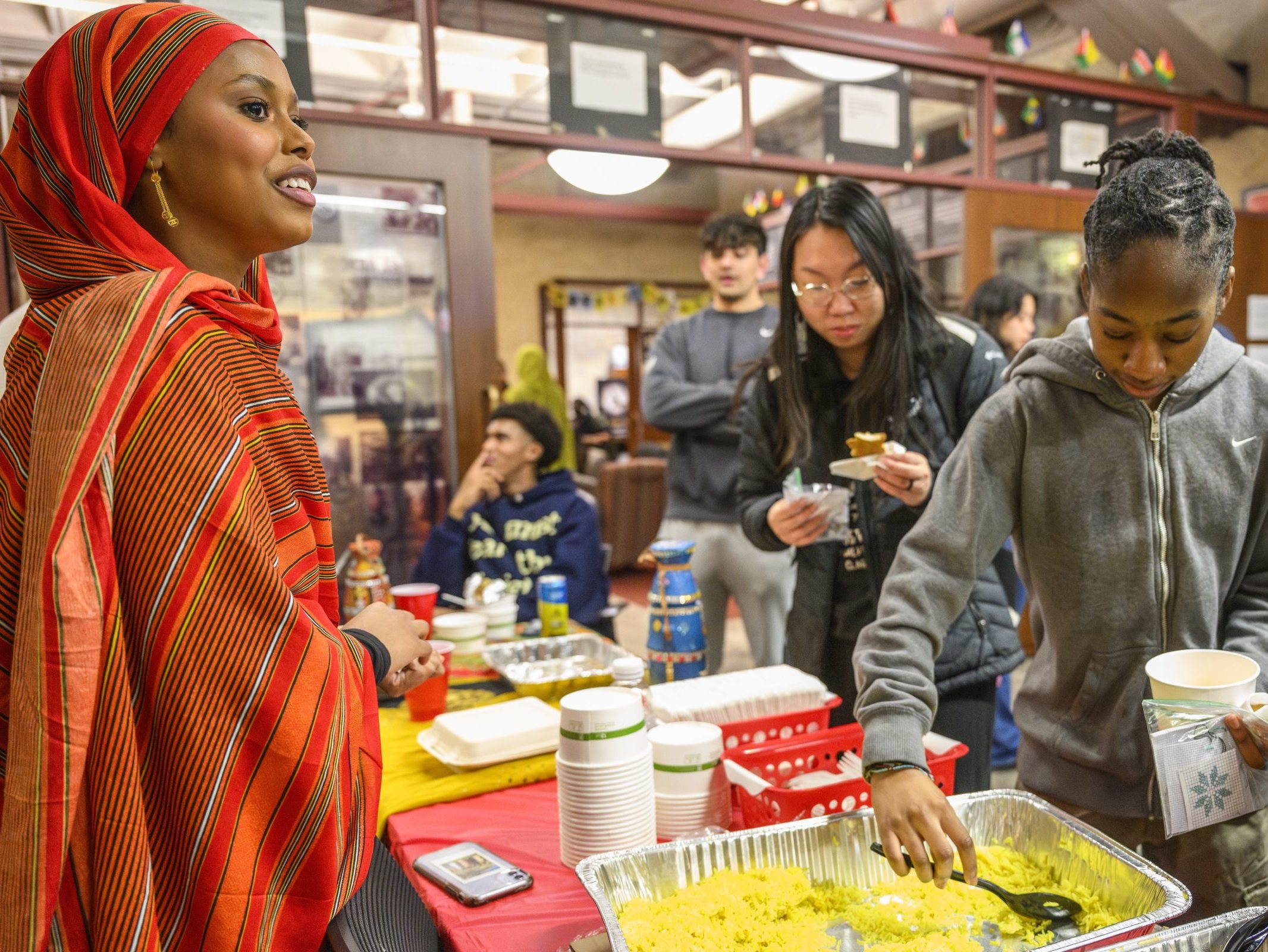 An ethnic woman at a booth where kids are taking food from her country to taste the cultural differences.