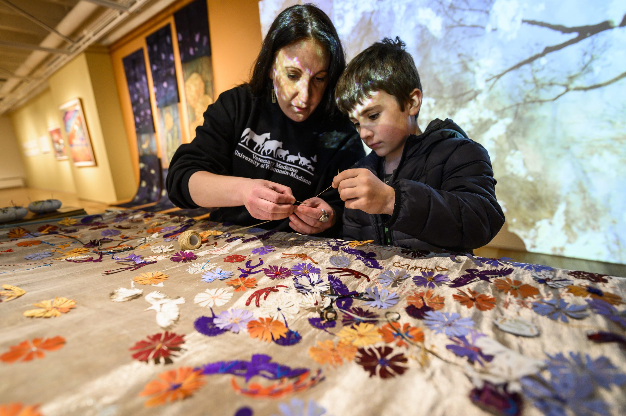 Woman and boy threading a needle to sew flower patterns on a quilt.