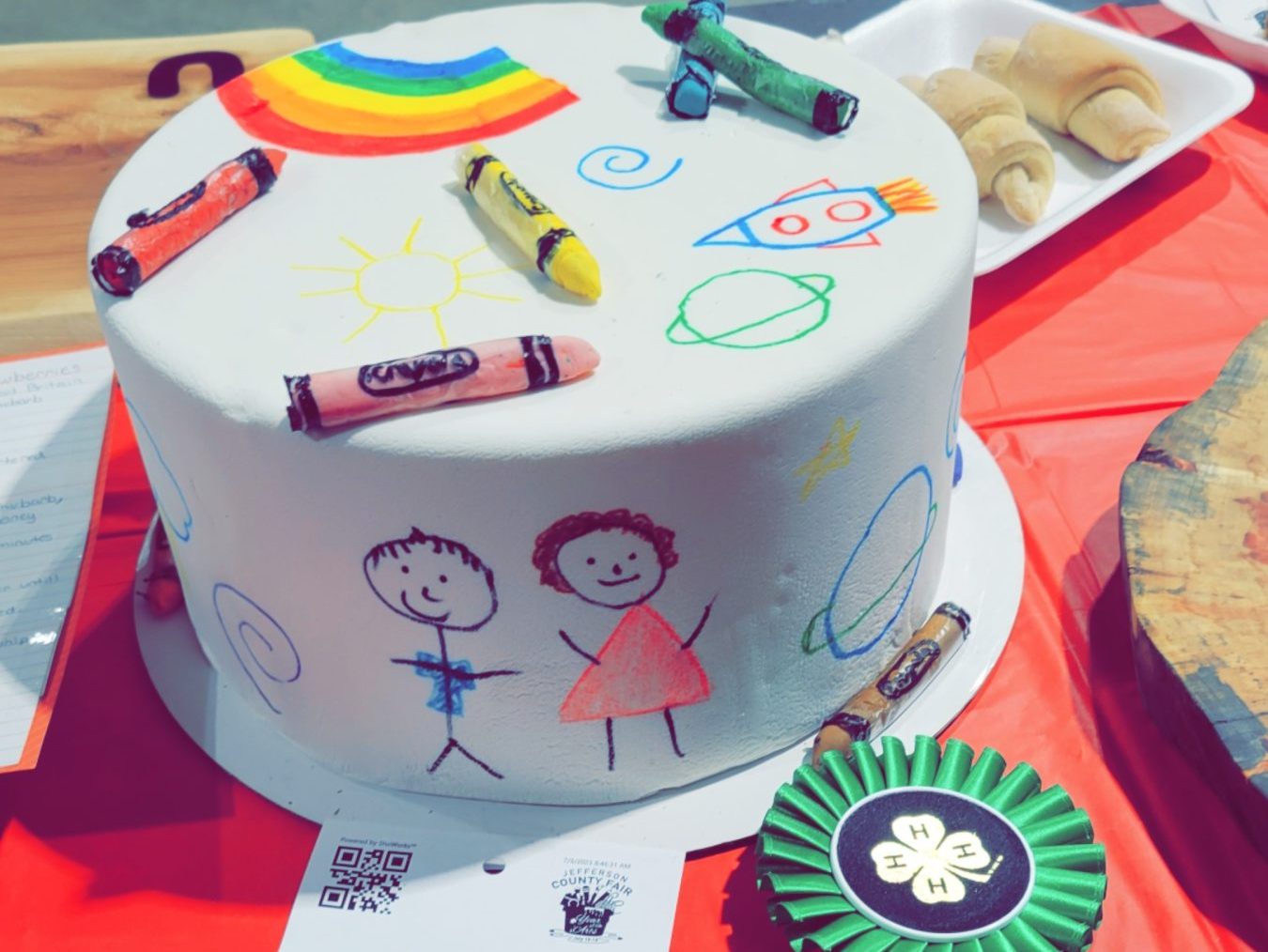 A cake with kids drawing on it with crayons on top. 
