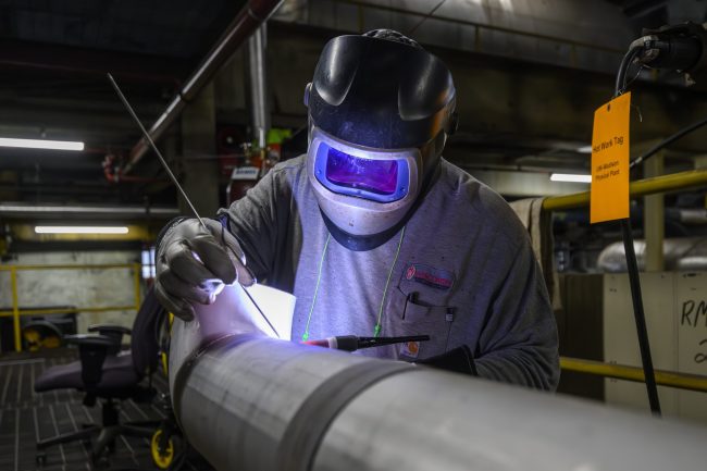 A person wearing welding gear while welding a parge metal tube