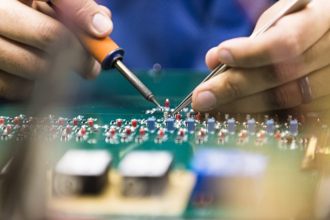 Hands with tools soldering a circuit board.