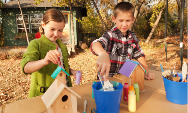 A girl and boy painting a birdhouse