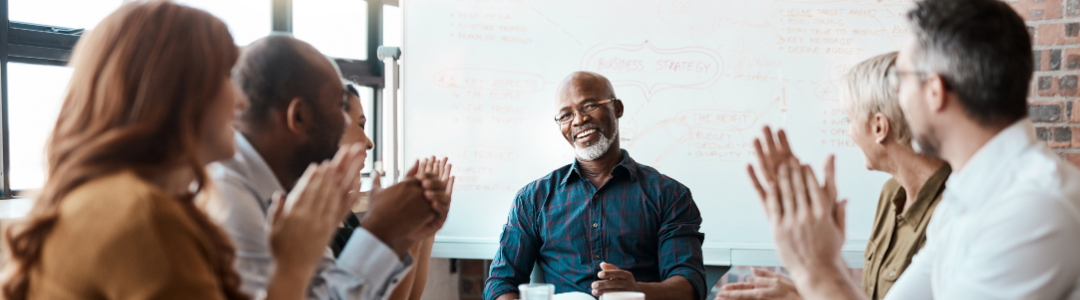 Group of people in a meeting with a man in the middle. The others are clapping.